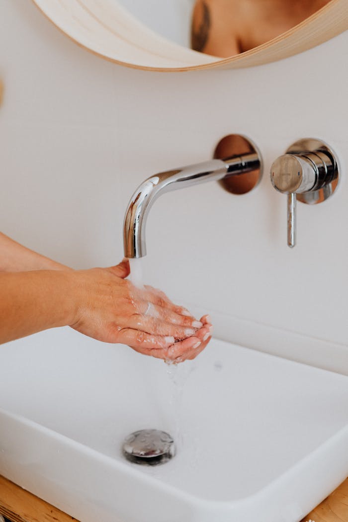 our-story A close-up of hands being washed in a modern bathroom with a stainless steel faucet.