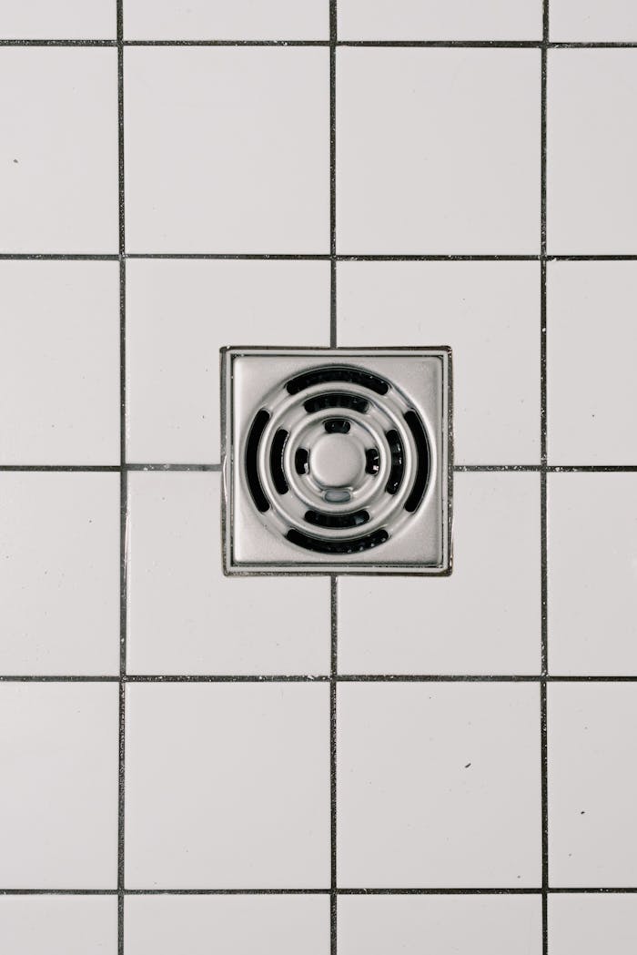 services-03 Top view of white ceramic tile floor with stainless steel square shaped cover of drain in contemporary shower