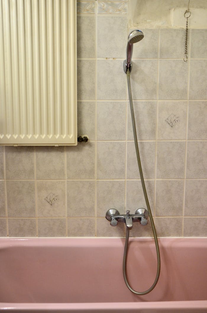 services-02 A vintage-style bathroom with a pink bathtub, silver shower head, and patterned tiles.
